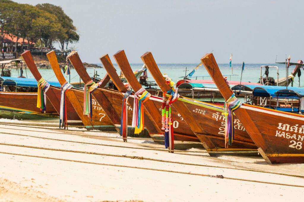 Vibrant longtail boats lined up on a sandy beach, perfect for travel and tourism imagery.