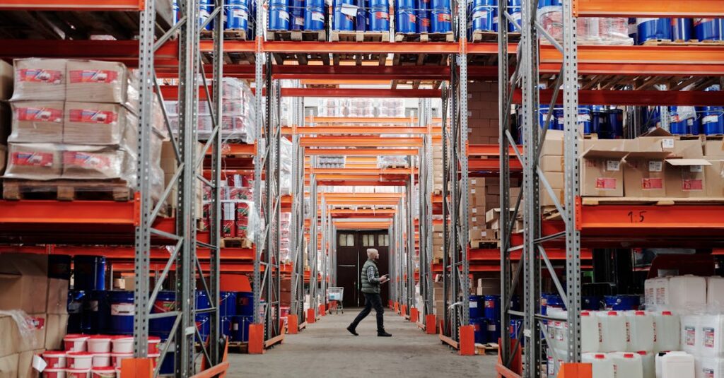 A man walking through a large industrial warehouse with stacked shelves filled with goods and products.